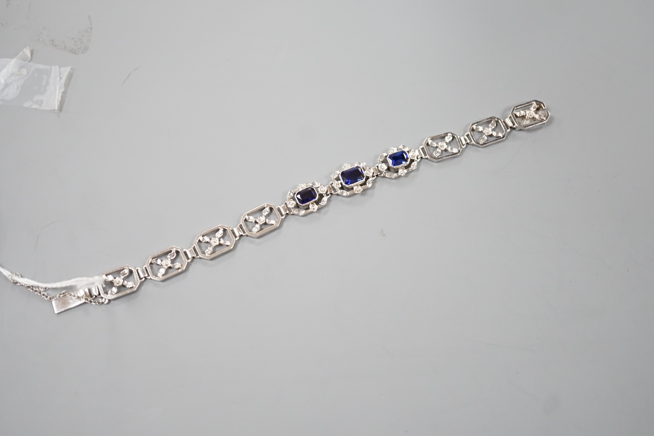 A modern 9ct white metal and three stone emerald cut synthetic sapphire set pierced link bracelet, approx. 18cm, gross weight 16.7 grams.